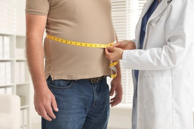 Photo of Nutritionist measuring overweight man's waist with tape in clinic, closeup