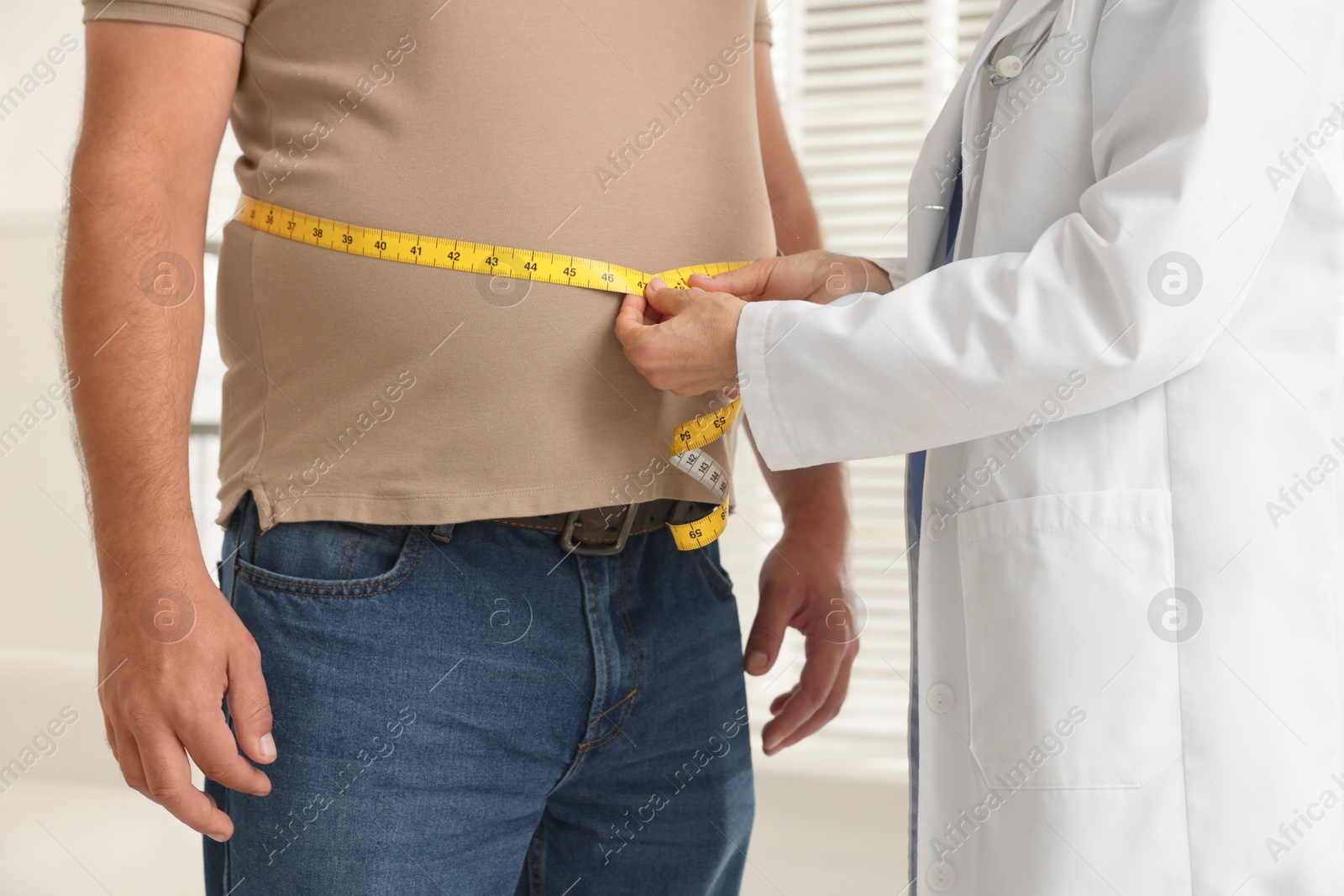 Photo of Nutritionist measuring overweight man's waist with tape in clinic, closeup