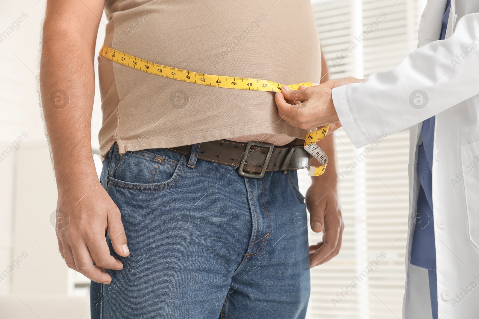 Photo of Nutritionist measuring overweight man's waist with tape in clinic, closeup