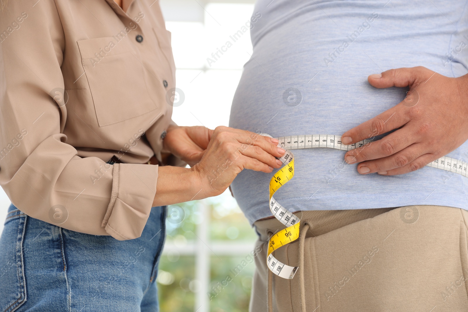 Photo of Nutritionist measuring overweight man's waist with tape in clinic, closeup