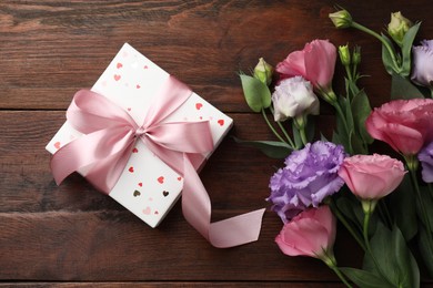 Photo of Gift box with bow and flowers on wooden table, flat lay