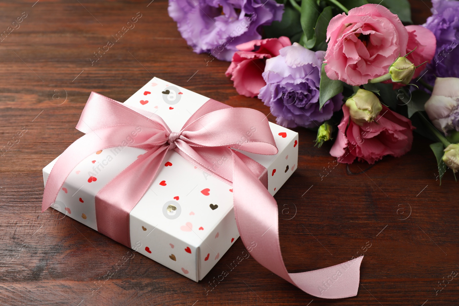 Photo of Gift box with bow and flowers on wooden table