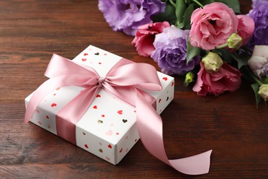 Photo of Gift box with bow and flowers on wooden table