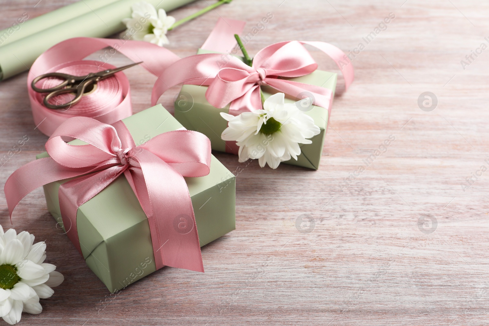 Photo of Gift boxes with bows, ribbon, scissors and flowers on pink wooden table, space for text