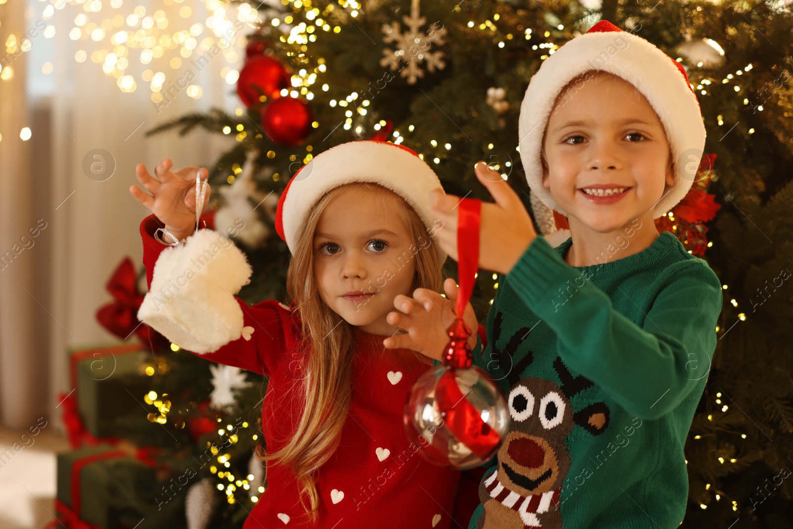 Photo of Little kids in Santa hats with Christmas ornaments at home