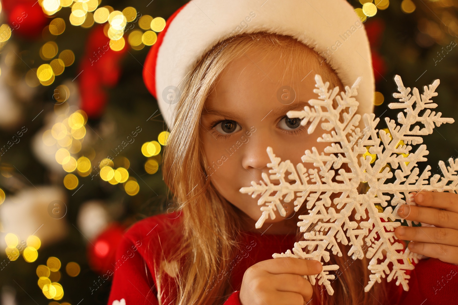 Photo of Little girl in Santa hat with decorative snowflake at home. Christmas celebration