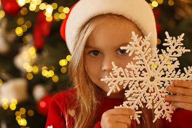 Photo of Little girl in Santa hat with decorative snowflake at home. Christmas celebration