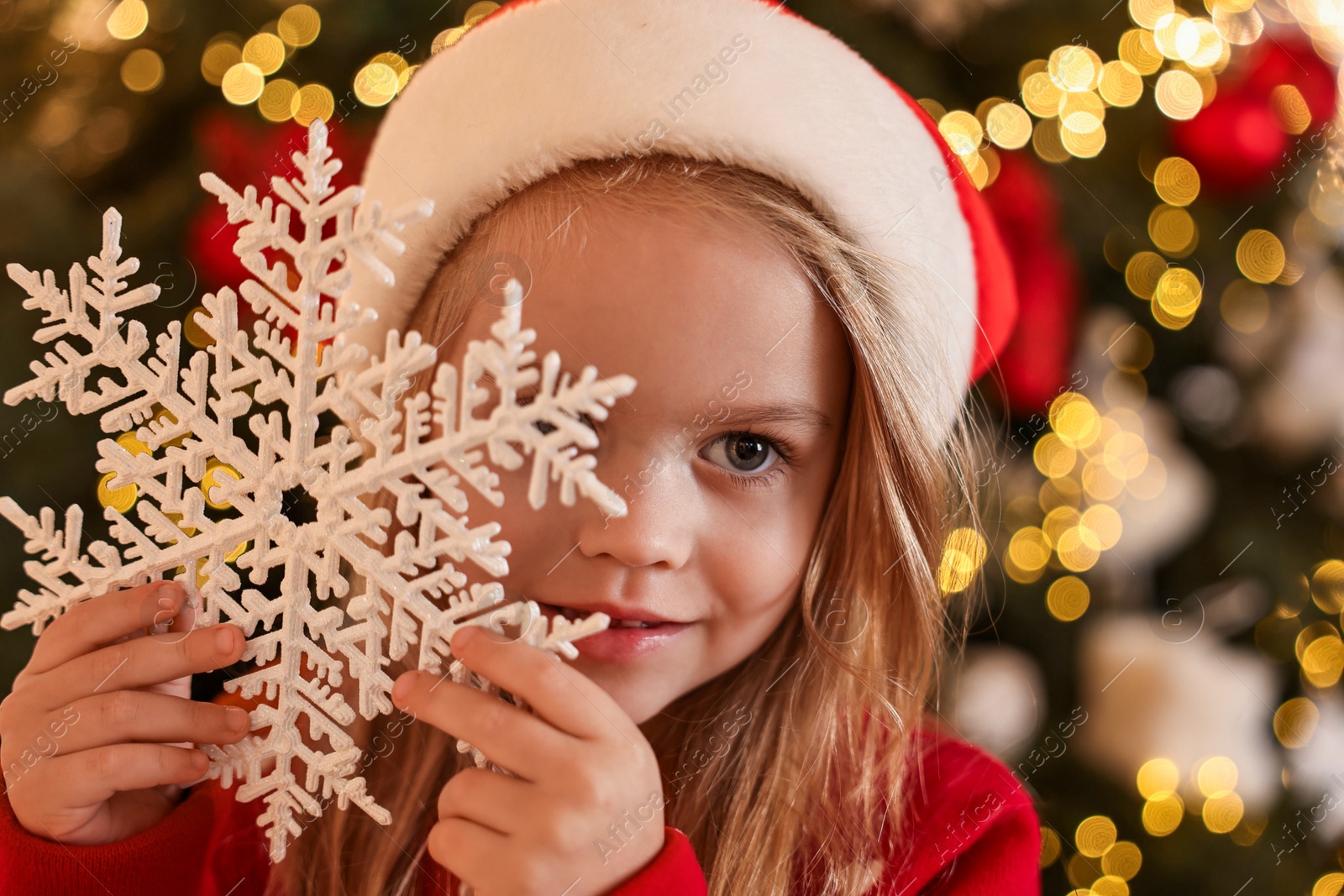 Photo of Little girl in Santa hat with decorative snowflake at home. Christmas celebration