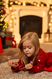 Photo of Little girl with candy canes on floor at home. Christmas celebration