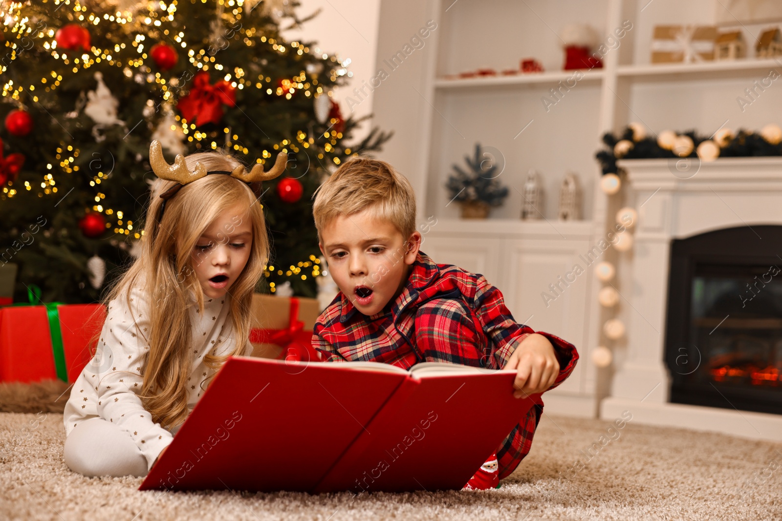 Photo of Little kids reading book on floor at home. Christmas celebration