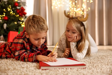 Photo of Little kids writing letter to Santa Claus on floor at home. Christmas celebration