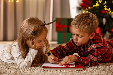 Photo of Little kids writing letter to Santa Claus on floor at home. Christmas celebration