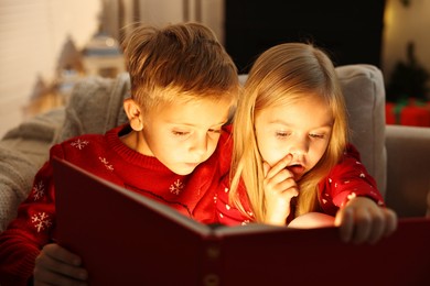 Photo of Little kids reading book on sofa at home. Christmas celebration