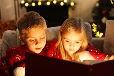 Photo of Little kids reading book on sofa at home. Christmas celebration