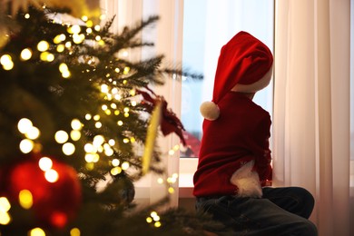 Photo of Little boy with Santa hat near window in room decorated for Christmas