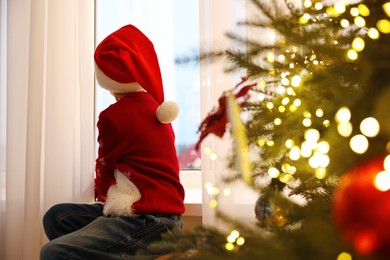 Photo of Little boy with Santa hat near window in room decorated for Christmas