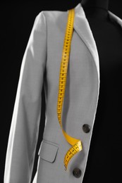 Photo of Female mannequin with gray jacket and measuring tape on black background, closeup