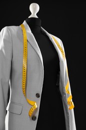 Photo of Female mannequin with gray jacket and measuring tape on black background, closeup