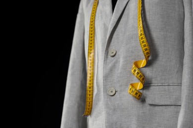 Photo of Male mannequin with jacket and measuring tape on black background, closeup. Space for text