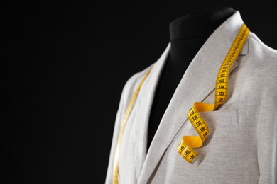 Photo of Male mannequin with jacket and measuring tape on black background, closeup. Space for text