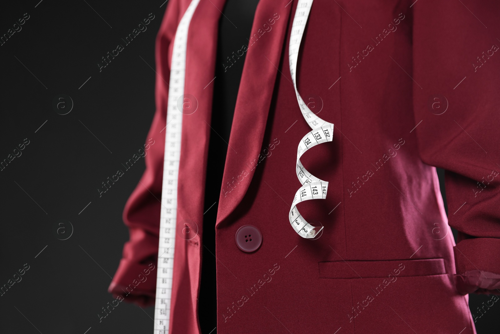 Photo of Female mannequin with stylish jacket and measuring tape on dark background, closeup