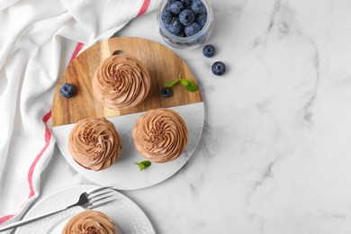 Photo of Tasty cupcakes with chocolate cream and blueberries on white marble table, flat lay. Space for text