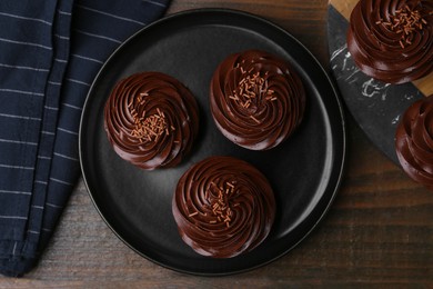 Photo of Tasty cupcakes with chocolate cream on wooden table, top view