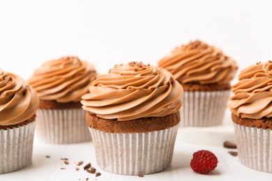 Photo of Tasty cupcakes with chocolate cream on white tiled table, closeup