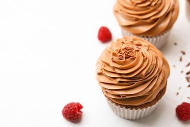 Photo of Tasty cupcakes with chocolate cream and raspberries on white tiled table, closeup. Space for text