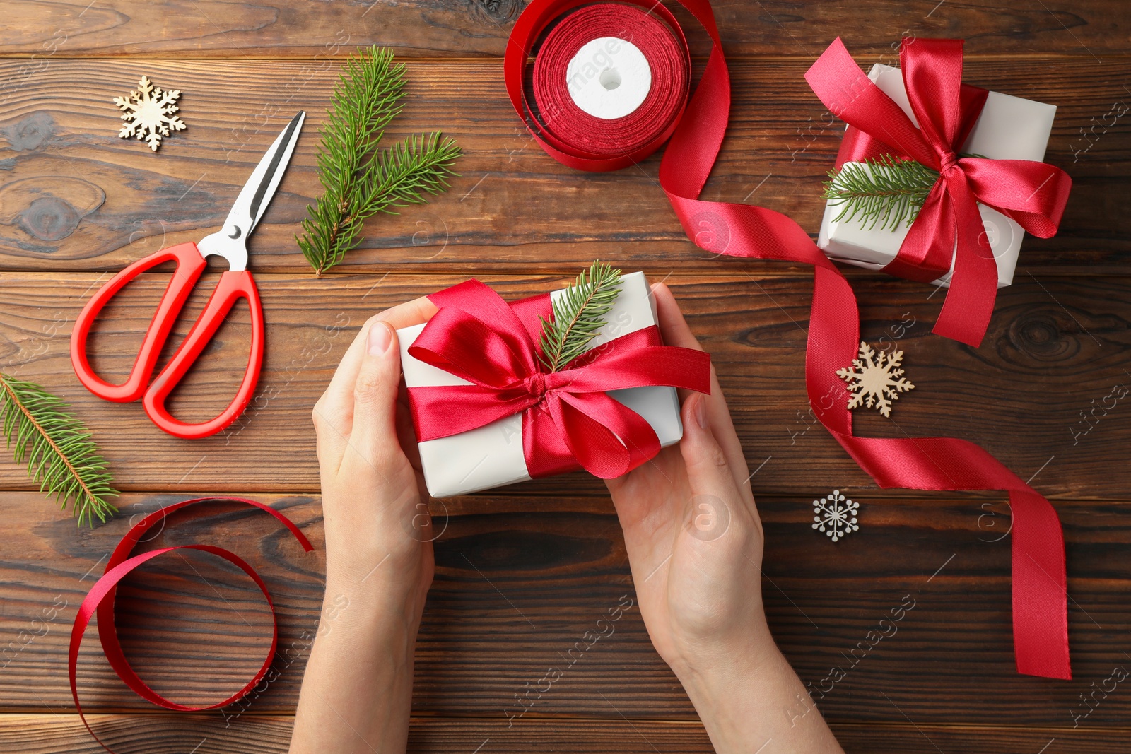 Photo of Woman holding gift box with red bow on wooden table, top view