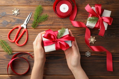 Photo of Woman holding gift box with red bow on wooden table, top view