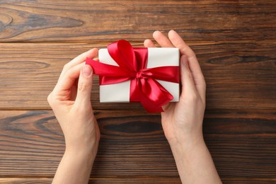 Photo of Woman holding gift box with red bow on wooden table, top view