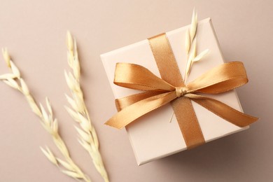 Photo of Gift box with golden bow and spikes on beige background, flat lay