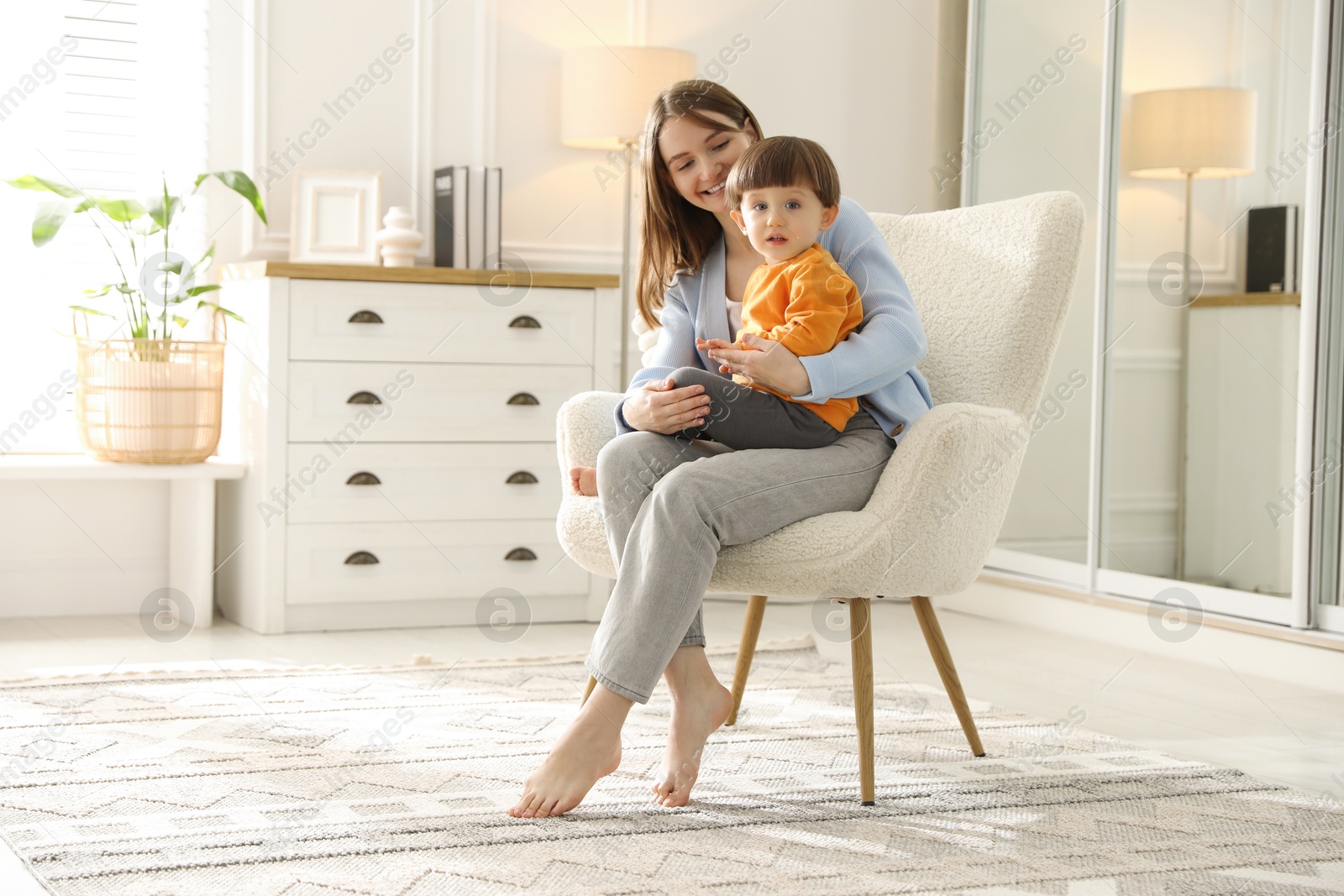 Photo of Happy mother with her little son sitting on armchair at home. Space for text