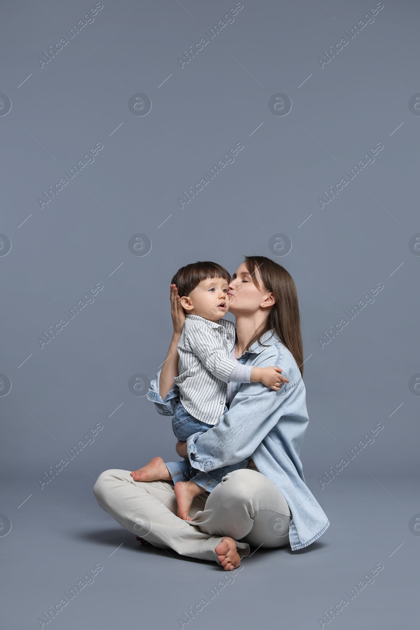 Photo of Mother kissing her little son on grey background. Space for text