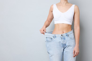 Photo of Weight loss. Woman wearing big jeans on light grey background, closeup. Space for text