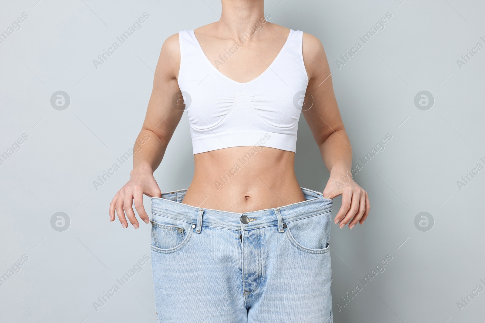 Photo of Weight loss. Woman wearing big jeans on light grey background, closeup