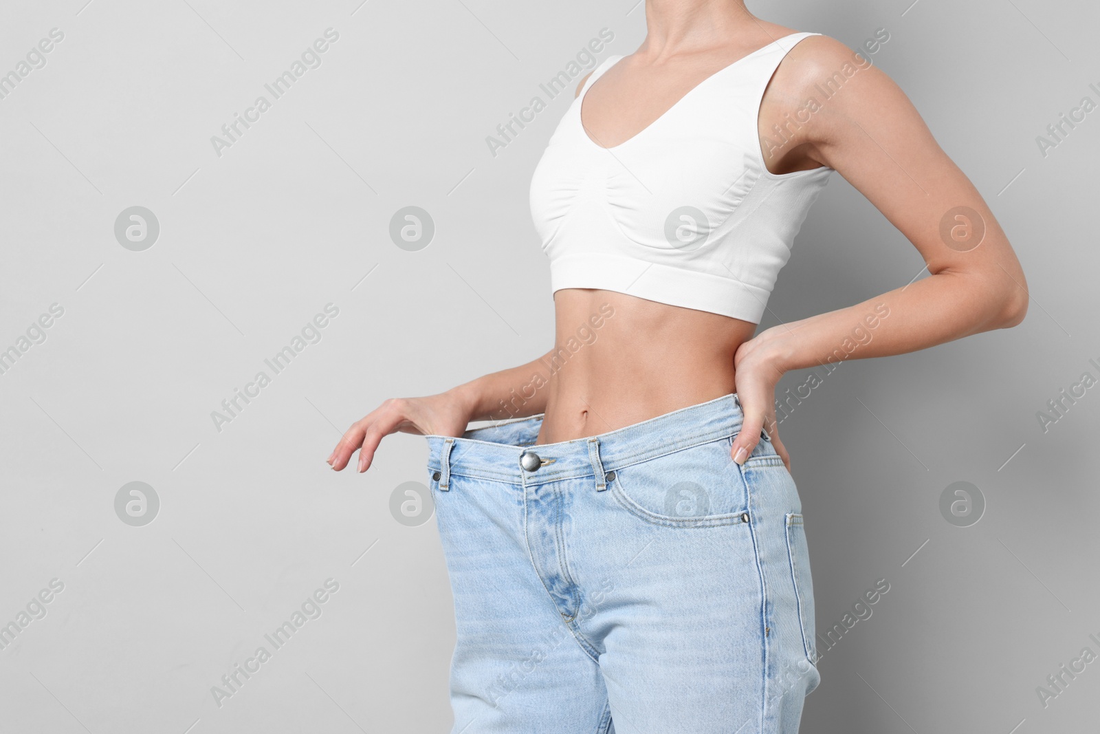 Photo of Weight loss. Woman wearing big jeans on light grey background, closeup. Space for text