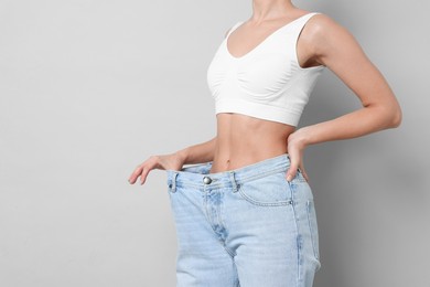 Photo of Weight loss. Woman wearing big jeans on light grey background, closeup. Space for text