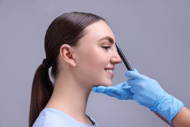 Photo of Doctor drawing marks on patient's nose for plastic surgery operation against grey background, closeup