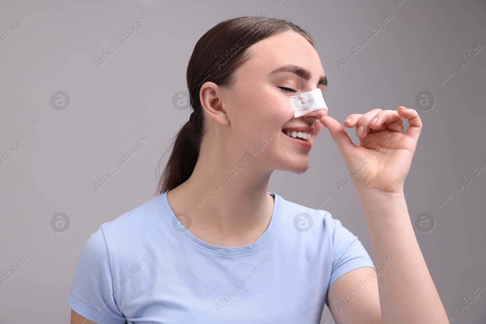 Photo of Woman with medical bandage on her nose after plastic surgery operation against grey background