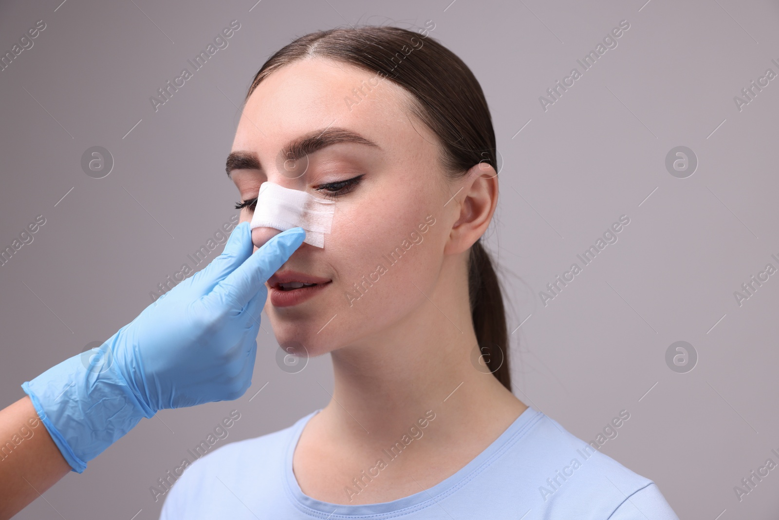 Photo of Doctor checking patient's nose after plastic surgery operation on grey background, closeup