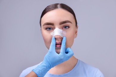 Photo of Doctor checking patient's nose after plastic surgery operation on grey background, closeup