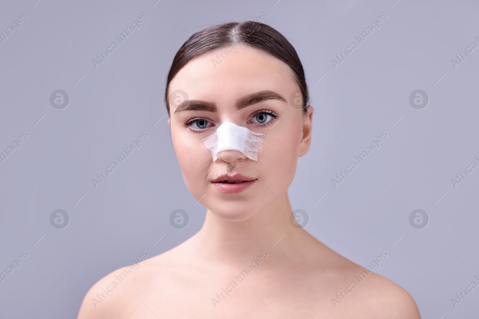 Photo of Woman with medical bandage on her nose after plastic surgery operation against grey background