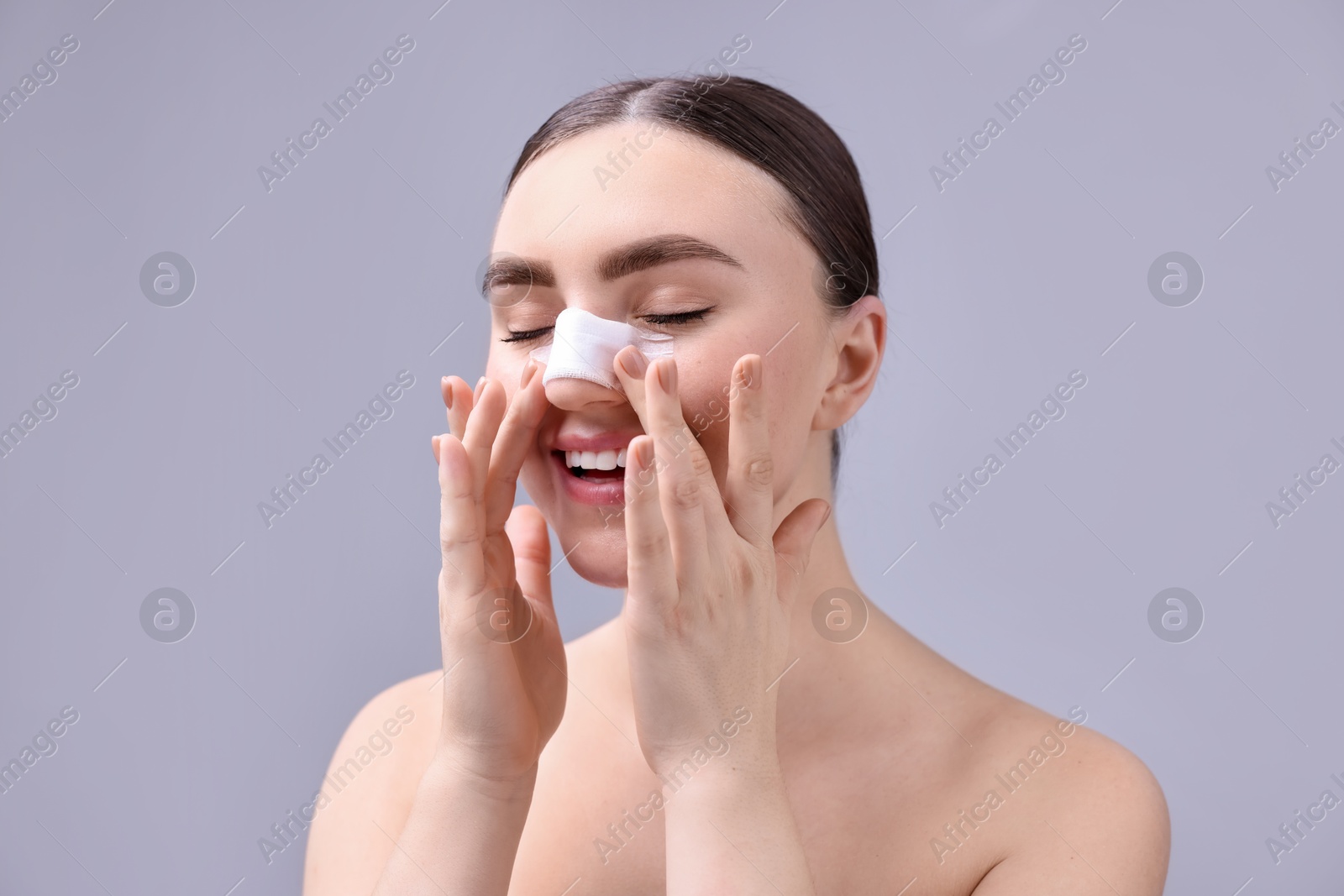 Photo of Woman with medical bandage on her nose after plastic surgery operation against grey background