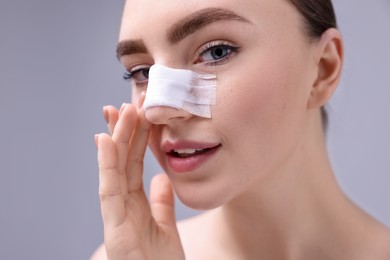 Photo of Woman with medical bandage on her nose after plastic surgery operation against grey background