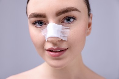 Photo of Woman with medical bandage on her nose after plastic surgery operation against grey background