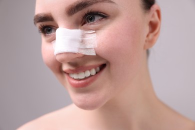 Photo of Woman with medical bandage on her nose after plastic surgery operation against grey background