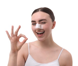 Photo of Woman with medical bandage on her nose after plastic surgery operation showing ok gesture against white background