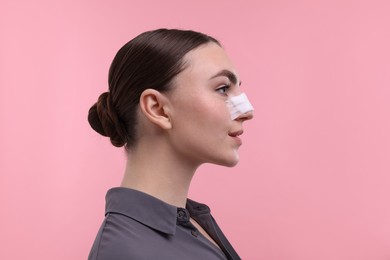 Photo of Woman with medical bandage on her nose after plastic surgery operation against pink background